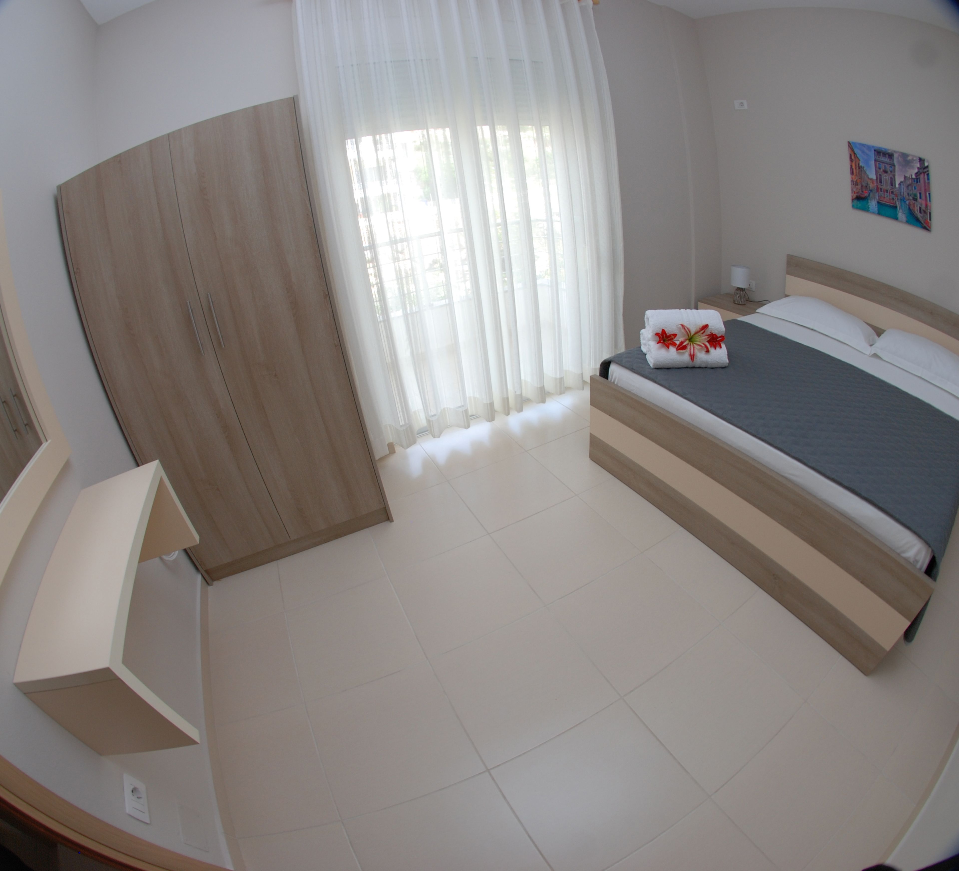 A bedroom with a bed, a desk, a chair, a window with curtains, and a painting on the wall.