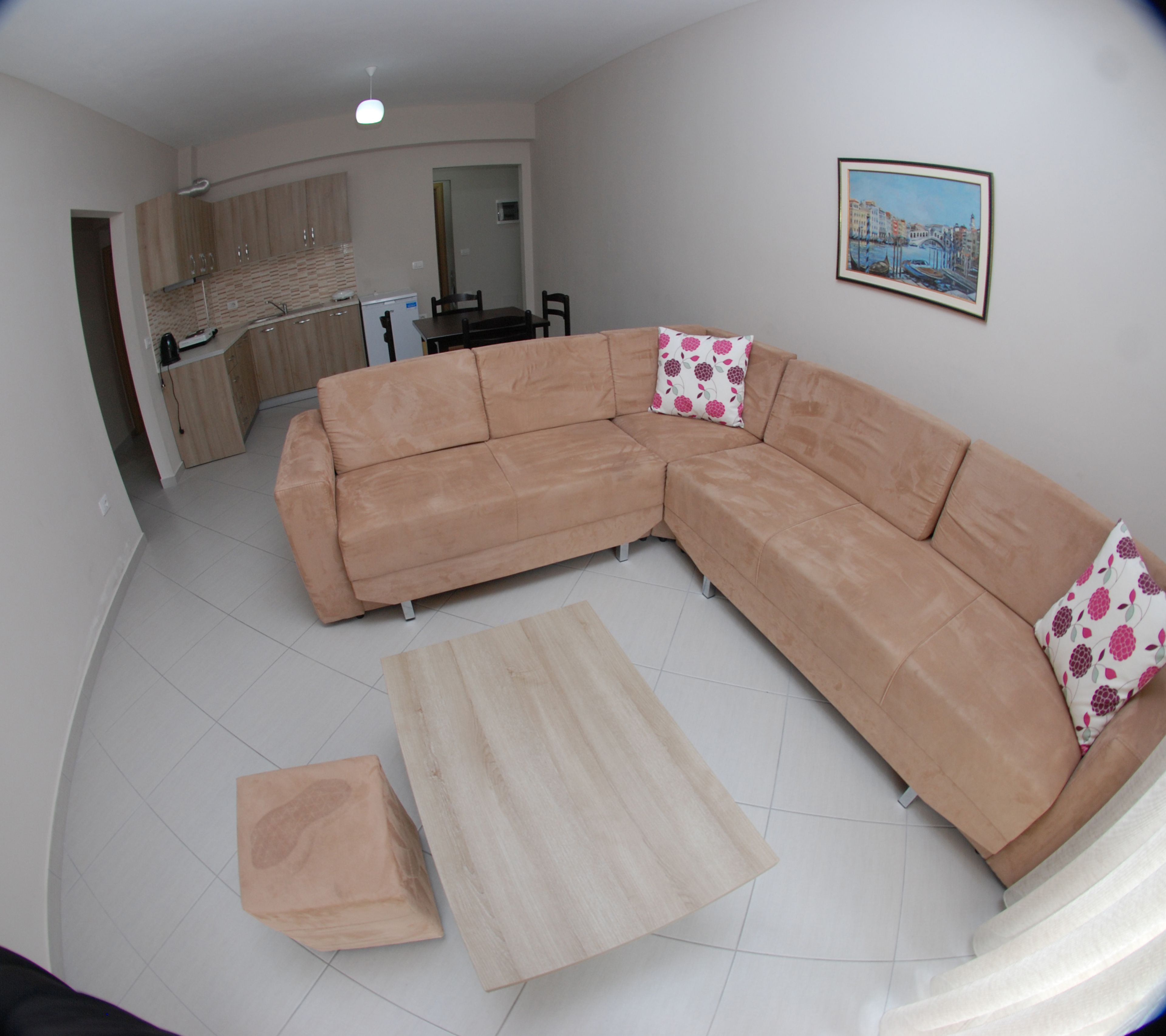 A living room with a L-shaped sectional sofa, a small wooden coffee table, and a dining area with a table and chairs.
