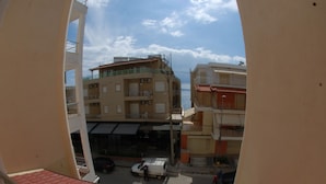 A view from a balcony with a red roof, overlooking a street with buildings and parked cars. - Wave Apartments Sarande (Sarandë)