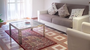 A living room with a sofa, a glass coffee table, a patterned rug, a floor lamp, and a window with curtains. - Roma - Via la Spezia 70 (Rome)