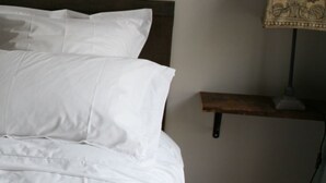 A neatly made bed with white linens and pillows, a bedside table with a lamp, and a wall-mounted shelf. - Chez Jules et Léonie (Valmondois)