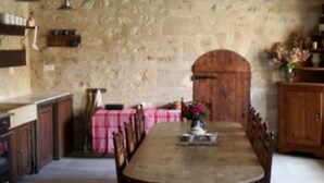A narrow, rustic kitchen with a long wooden table, a stone wall, and a wooden door. - Chez Jules et Léonie (Valmondois)