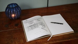 An open sketchbook with a pen on a wooden table. - Chez Jules et Léonie (Valmondois)