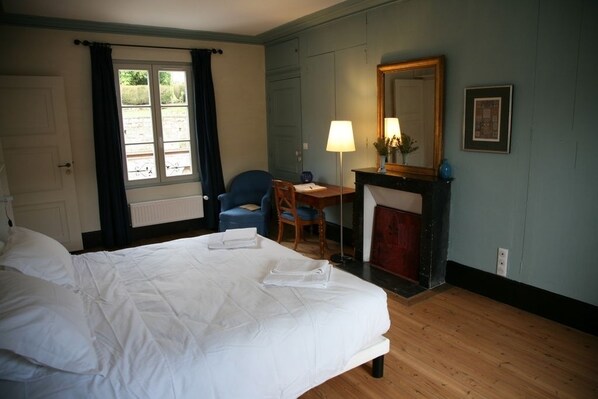 A hotel room with a large bed, a desk with a lamp, a chair, a fireplace, and a window with curtains. - Chez Jules et Léonie (Valmondois)