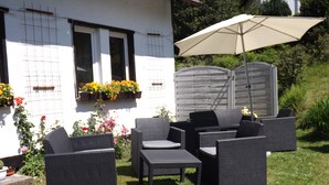 An outdoor seating area with wicker furniture, a large umbrella, and flower boxes on the building's exterior. - Pension Sonneneck (Osterode am Harz)