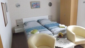 A bedroom with two beds, a wardrobe, two chairs, a small table with a clock, and a wall with two decorative plates. - Pension Sonneneck (Osterode am Harz)
