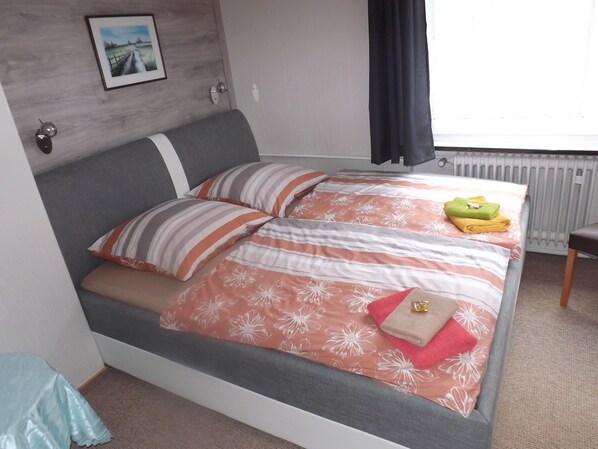 A neatly made bed with striped pillows, a floral bedspread, and towels on the side. - Pension Sonneneck (Osterode am Harz)