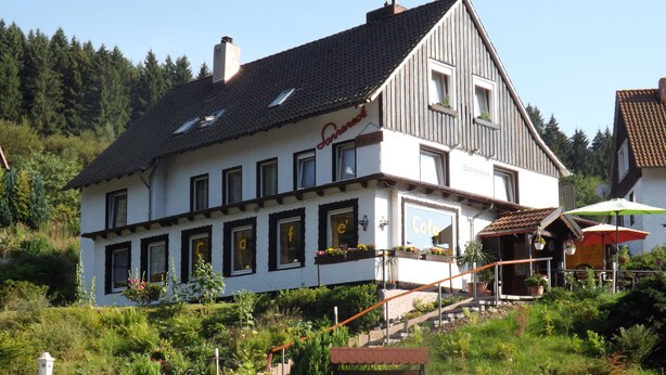 A two-story building with a cafe and pension signs, surrounded by greenery and a staircase leading up to the entrance. - Pension Sonneneck (Osterode am Harz)