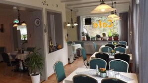 A restaurant with multiple dining tables and chairs, a counter with a coffee machine, and potted plants. - Pension Sonneneck (Osterode am Harz)