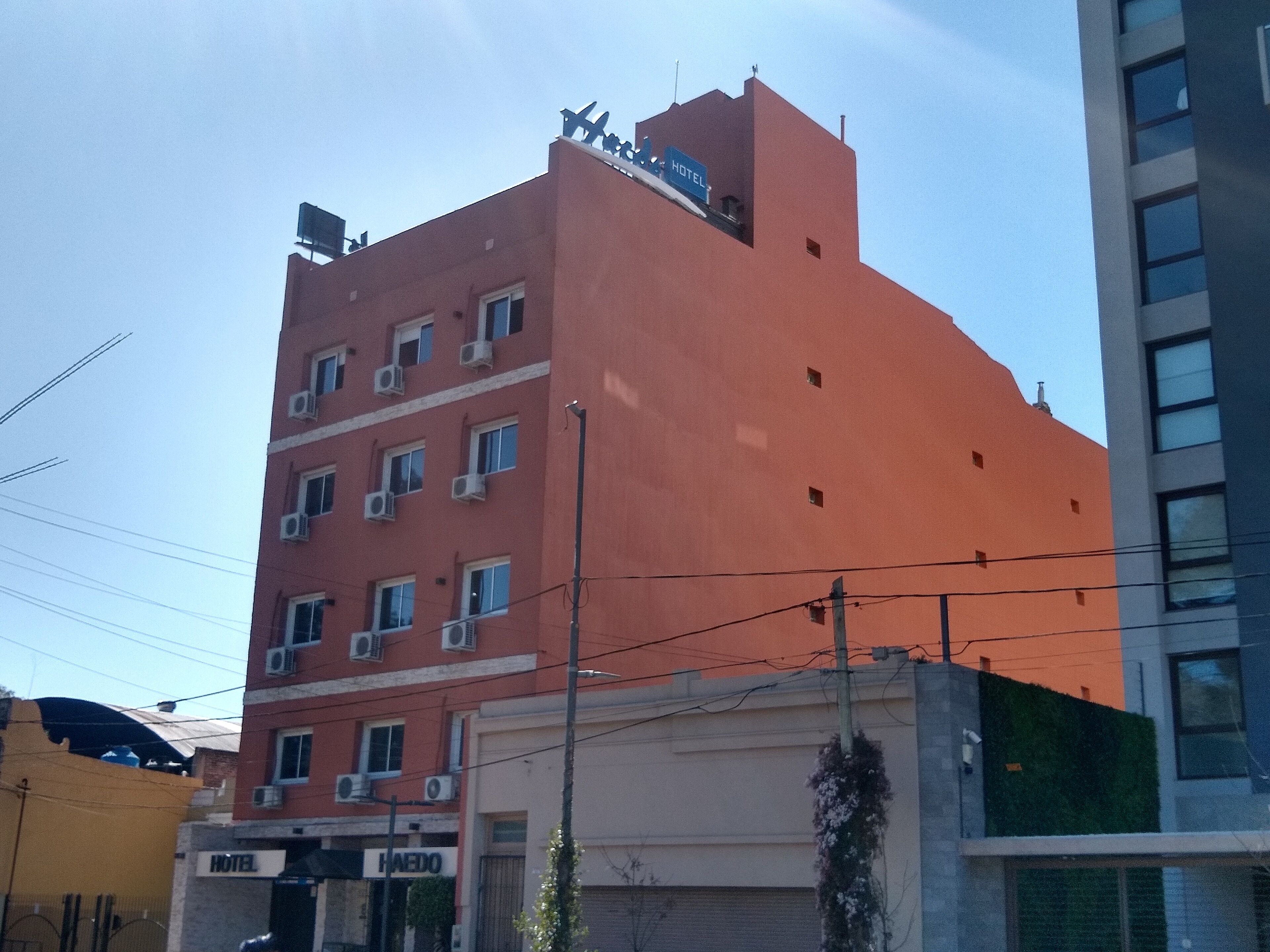 A multi-story hotel with a red facade, multiple air conditioning units, and a sign indicating it is a hotel.