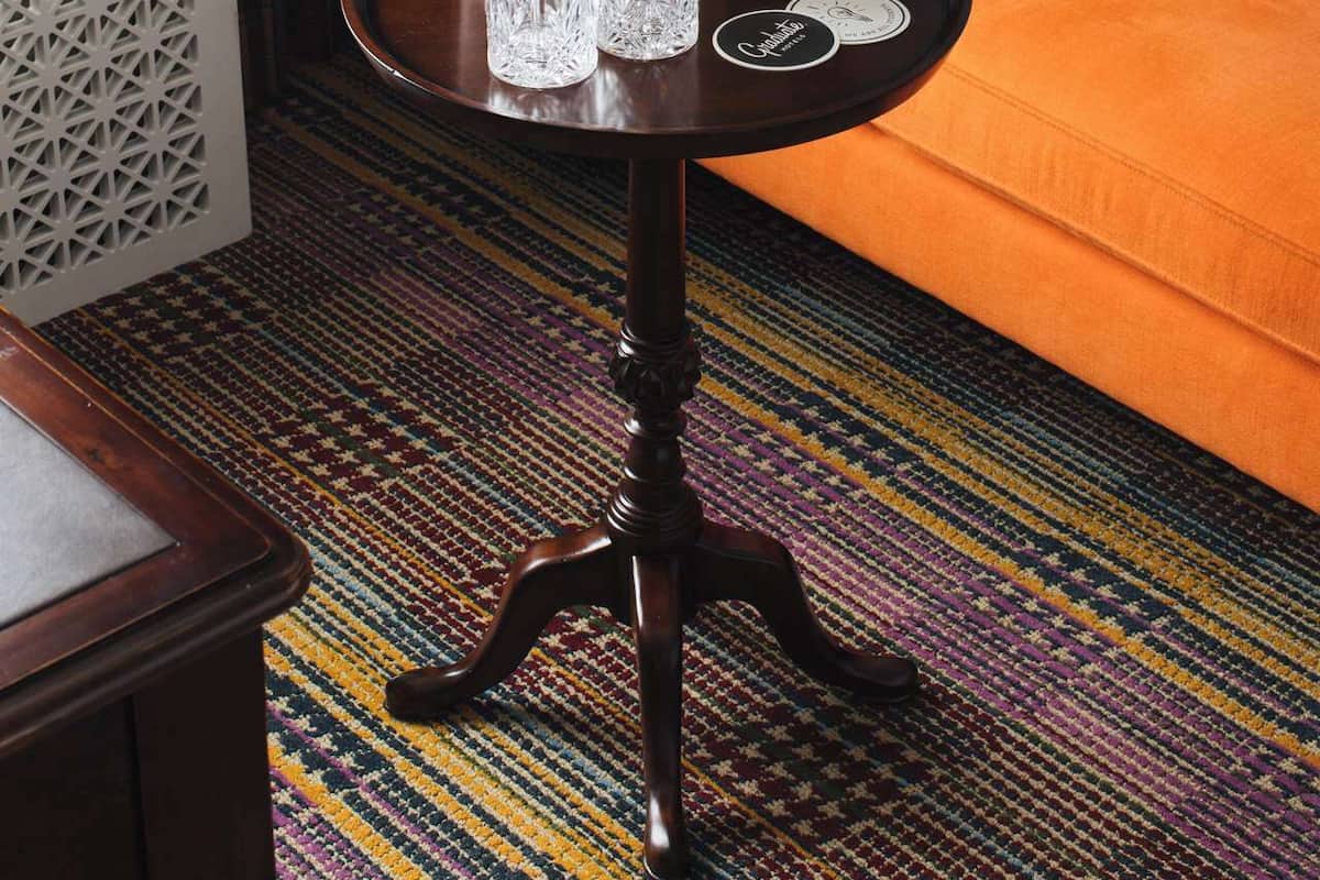 Ein Zimmer mit einem orangefarbenen Sofa, einem kleinen runden Tisch mit einer Flasche und Gläsern sowie einem gemusterten Teppich.