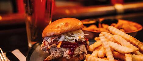 A plate with a pulled pork sandwich and fries, a glass of beer, and a fork on a table.
