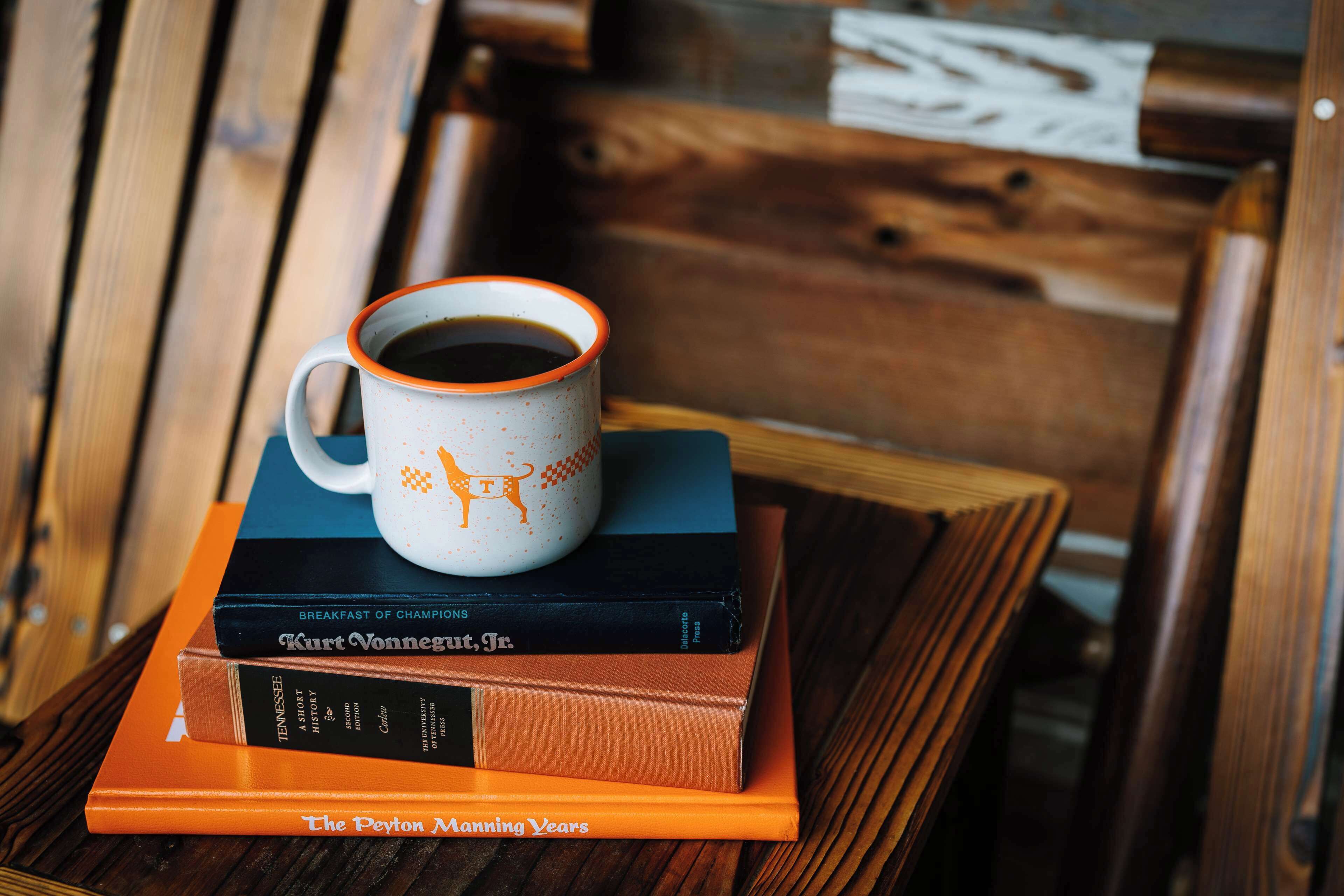 A stack of books with a coffee mug on top, placed on a wooden table.