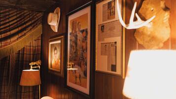 A room with wooden paneling, a plaid curtain, a framed portrait, a lamp, and a mounted antler.