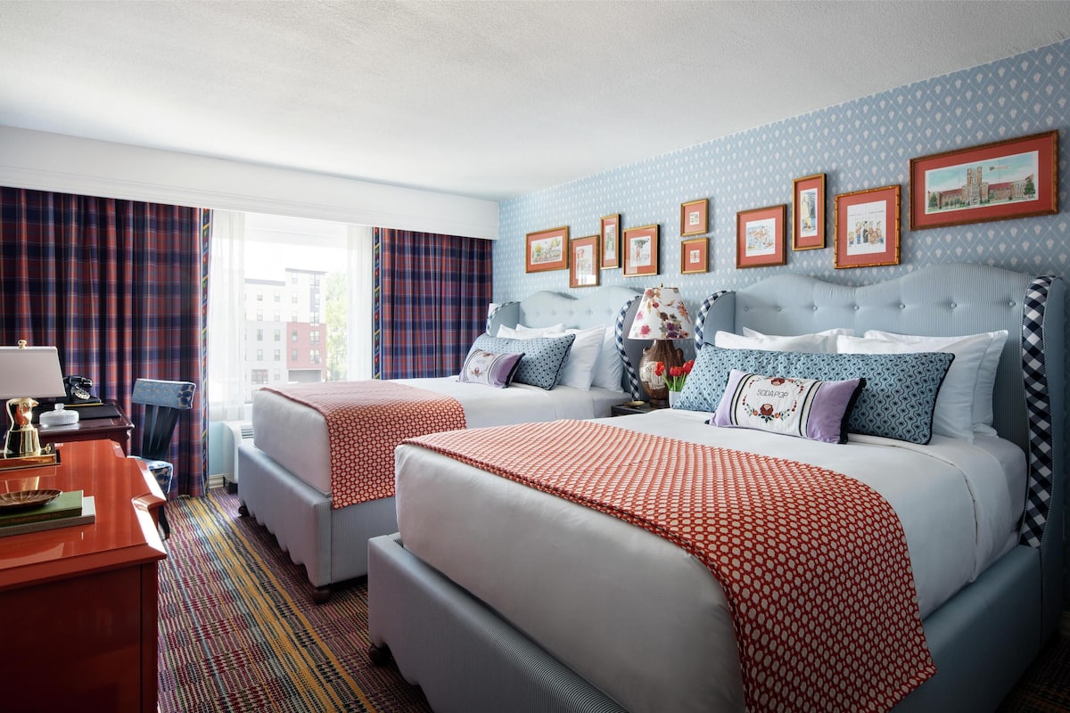 Ein Hotelzimmer mit zwei Betten, einem Schreibtisch und einem Fenster mit Vorhängen.