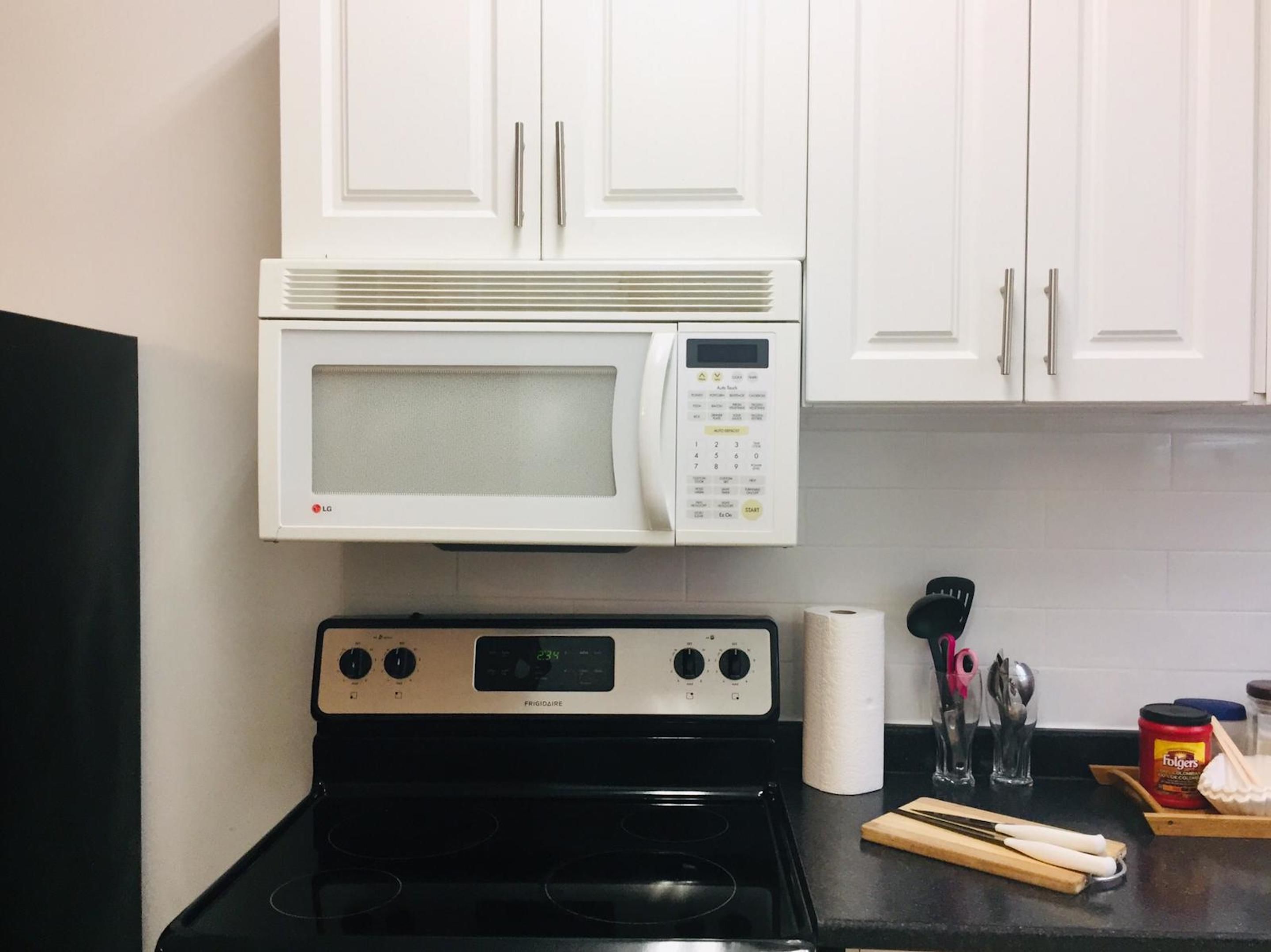 A kitchen with white cabinets, a black stove, a microwave, and various kitchen utensils on the counter.