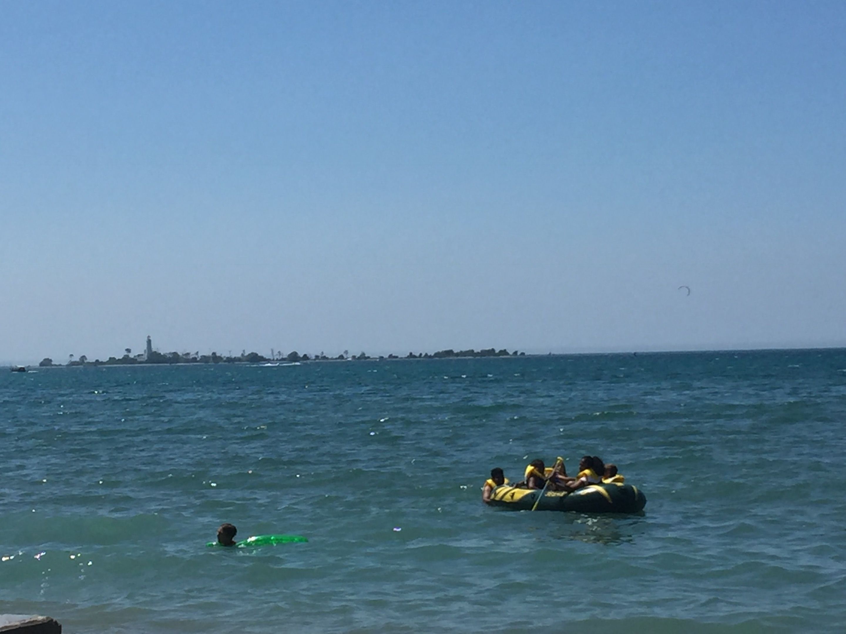 Un grupo de personas en una balsa en el océano, con una costa distante.