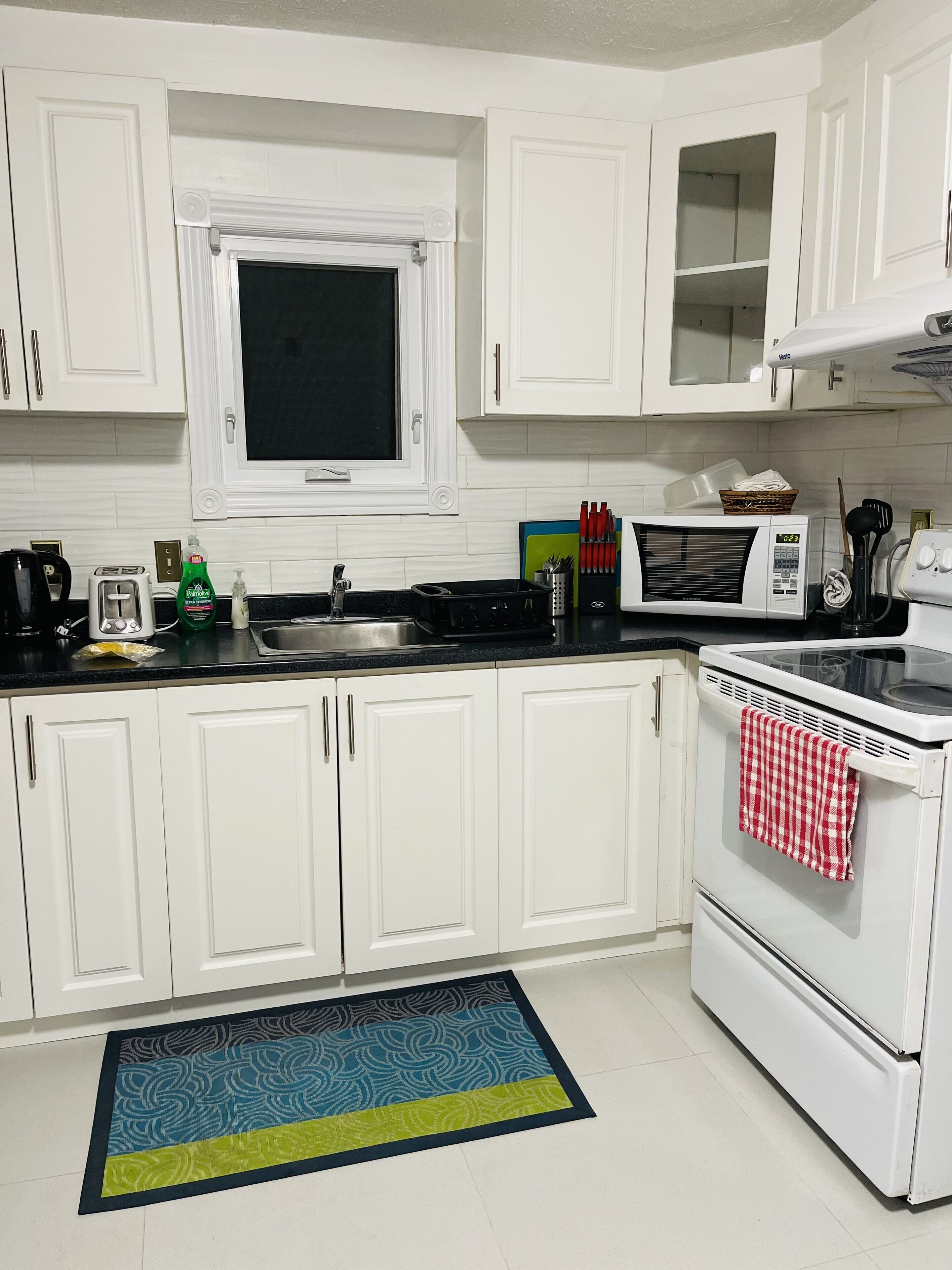 A kitchen with white cabinets, a microwave, a stove, a sink, and a window above the sink.