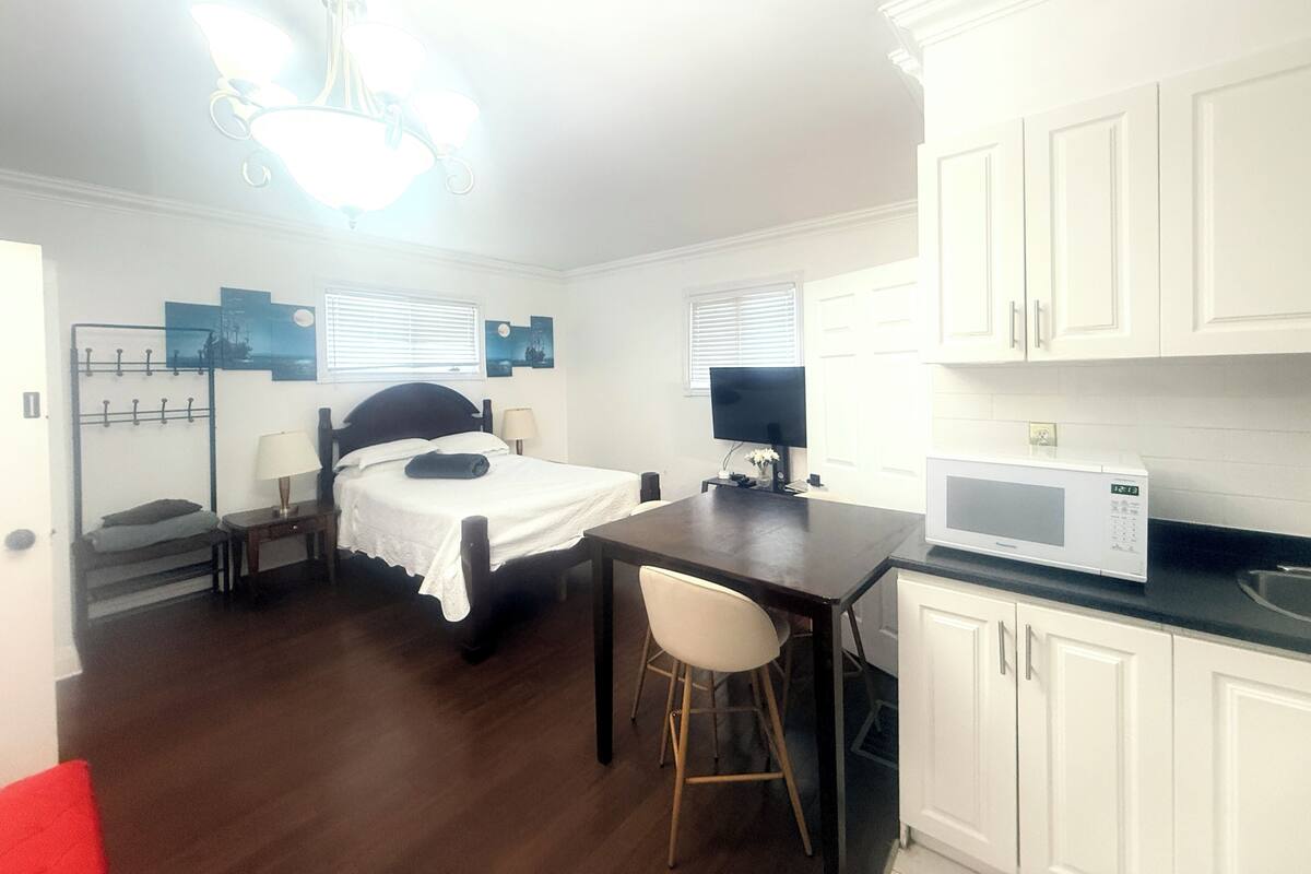 A small, well-lit room with a bed, a desk, a chair, a TV, and a microwave.