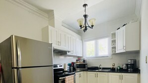 Une cuisine avec des meubles blancs, des appareils électroménagers en acier inoxydable, une fenêtre et un lustre.