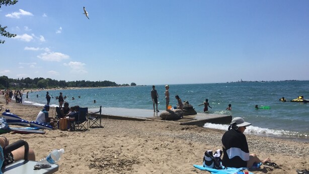 Une scène de plage où l’on voit des gens se détendre sur des chaises et des serviettes, un ciel dégagé et une mer calme.