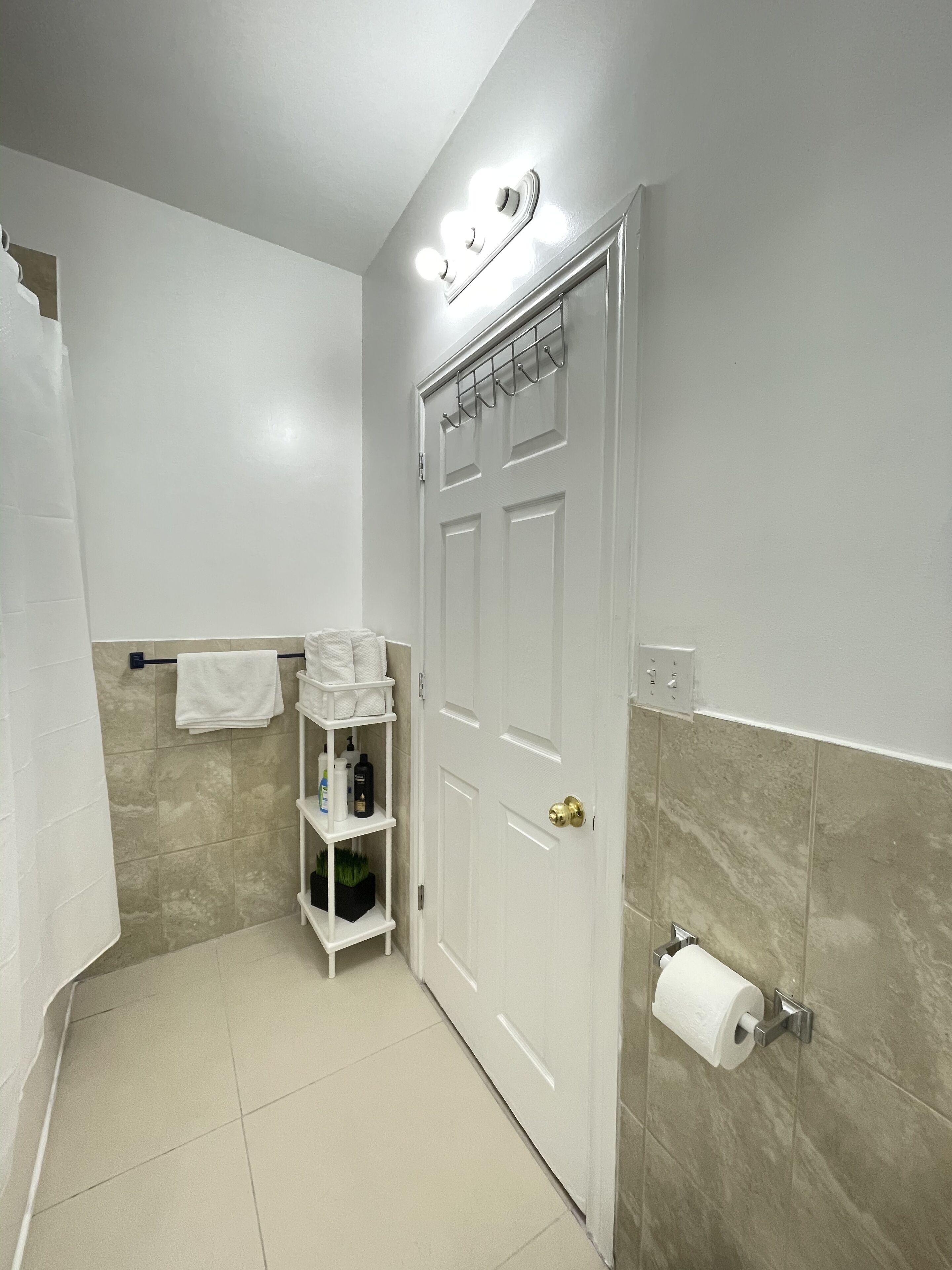 A bathroom with a white door, a towel rack, a shelf with toiletries, and a toilet paper holder.