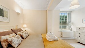 Een slaapkamer met een bed, een bedlampje, een raam met zonwering, een radiator en een dressoir.