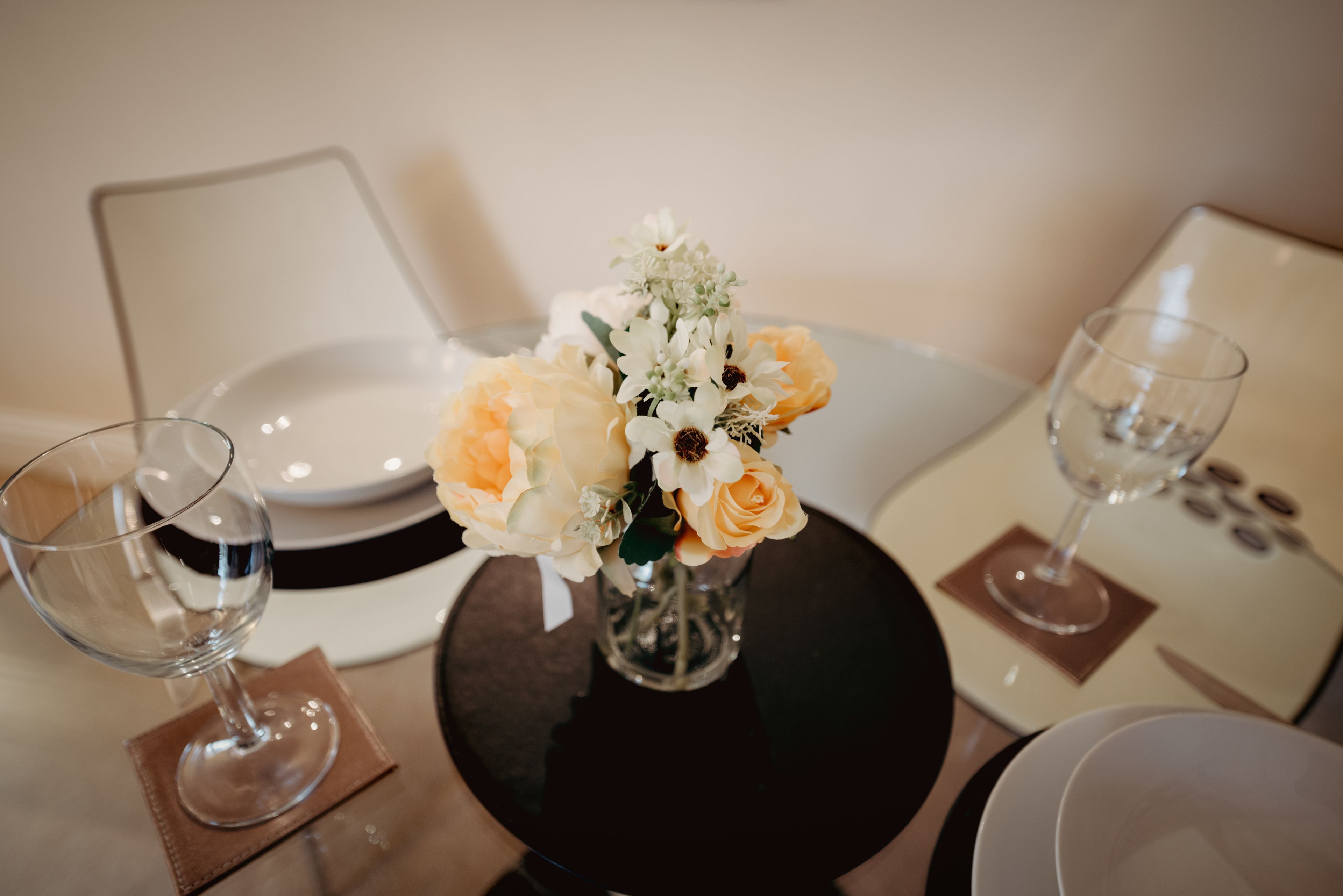 A dining table with a vase of flowers, two wine glasses, and a plate.