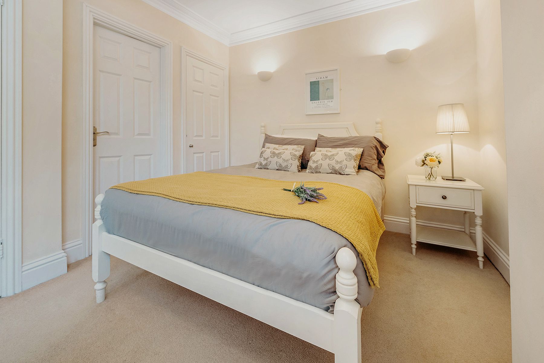A bedroom with a bed, bedside table, lamp, and a framed picture on the wall.