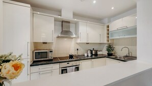 Een moderne keuken met witte kasten, een magnetron, een fornuis en een spoelbak.