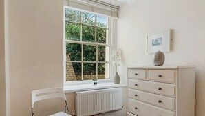 Een kamer met een radiator, een raam met uitzicht op groen, een witte kapstok en een witte stoel.