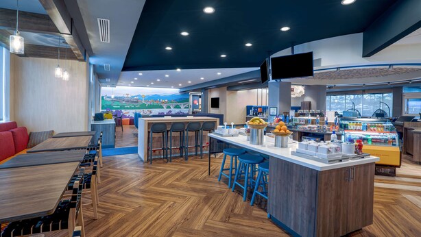 A modern restaurant with a long communal table, a bar area, and a counter with stools. - Tru by Hilton Knoxville North I75 (Knoxville)