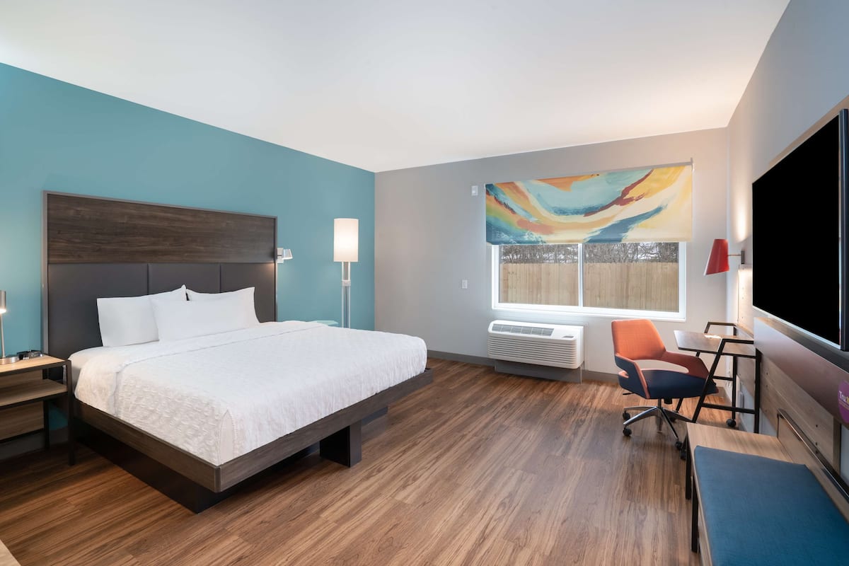 A modern hotel room with a large bed, a desk, a chair, and a TV.
