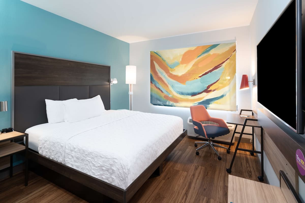 A modern hotel room with a large bed, a desk, and a colorful abstract painting on the wall.