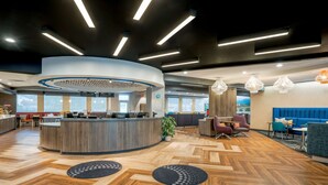 A modern hotel lobby with a curved reception desk, seating area with sofas and chairs, and a wooden herringbone floor. - Tru by Hilton Knoxville North I75 (Knoxville)