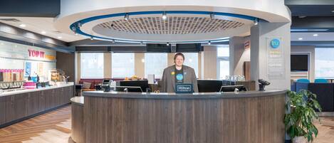 A modern hotel reception area with a curved desk, a nameplate, and a large window.