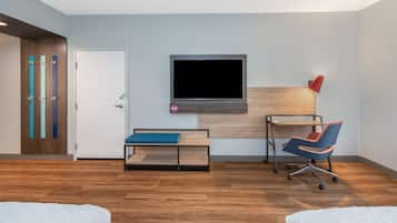 A modern room with a wooden floor, a bed, a desk with a chair, a TV mounted on the wall, and a door with a colorful panel.