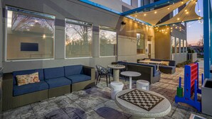 An outdoor seating area with a blue sofa, wicker chairs, and a round table. - Tru by Hilton Knoxville North I75 (Knoxville)
