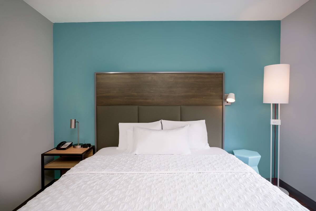 A hotel room with a bed, a nightstand with a lamp, and a bedside table with a phone.