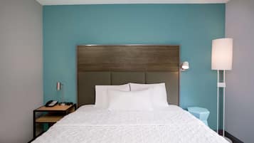 A hotel room with a bed, a nightstand with a lamp, and a bedside table with a phone.