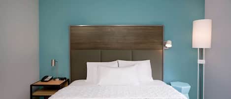 Una habitación de hotel con una cama, una mesita de noche con lámpara y una mesita junto a la cama con teléfono.