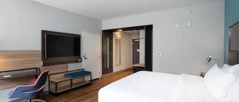 A modern hotel room with a large bed, a desk with a chair, a flat-screen TV, and a walk-in closet.