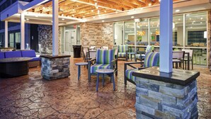 An outdoor patio area with stone flooring, wooden tables, chairs, and a stone fireplace. - Home2 Suites by Hilton Georgetown (Georgetown)