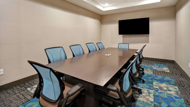 A conference room with a long table, blue chairs, a flat-screen TV on the wall, and a patterned carpet. - Home2 Suites by Hilton Georgetown (Georgetown)