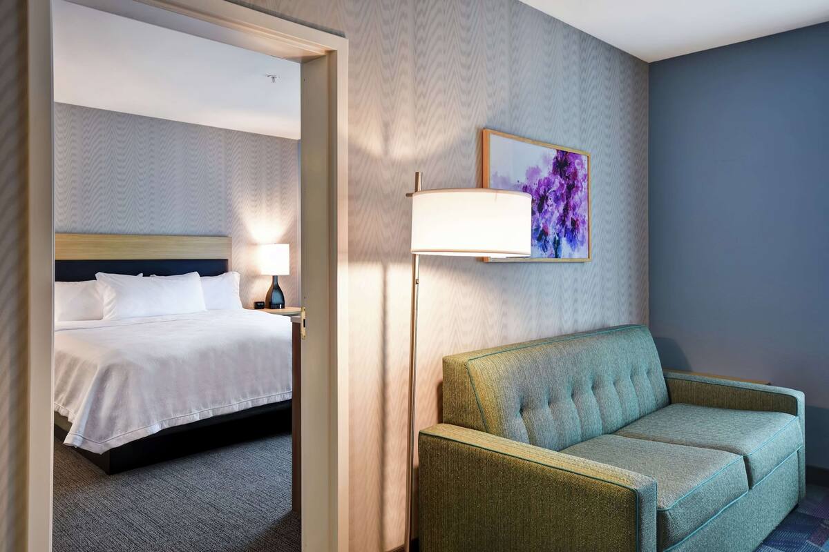 Une chambre d’hôtel avec un lit, un canapé vert, une lampe et un tableau au mur.