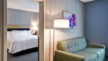 A hotel room with a bed, a green sofa, a lamp, and a painting on the wall.