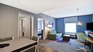 A modern hotel room with a dining area, a sofa, a TV, and a window with blinds. - Home2 Suites by Hilton Georgetown (Georgetown)