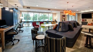 A modern lounge area with a sofa, chairs, tables, and a TV screen. - Home2 Suites by Hilton Georgetown (Georgetown)