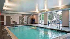 An indoor swimming pool with clear water, a tiled edge, and a sunlit area with outdoor seating visible through large windows. - Home2 Suites by Hilton Georgetown (Georgetown)