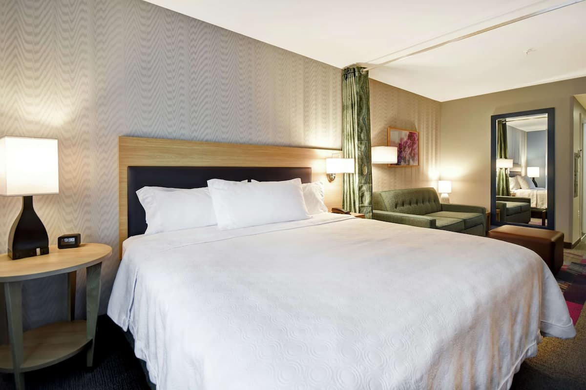 Une chambre d’hôtel avec un grand lit, une table de chevet avec une lampe, une chaise et un miroir.